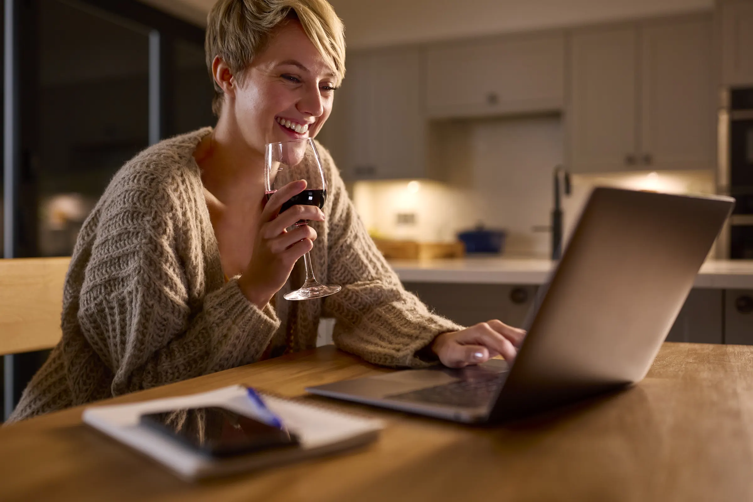 A woman at her kitchen table at night, browsing on a laptop